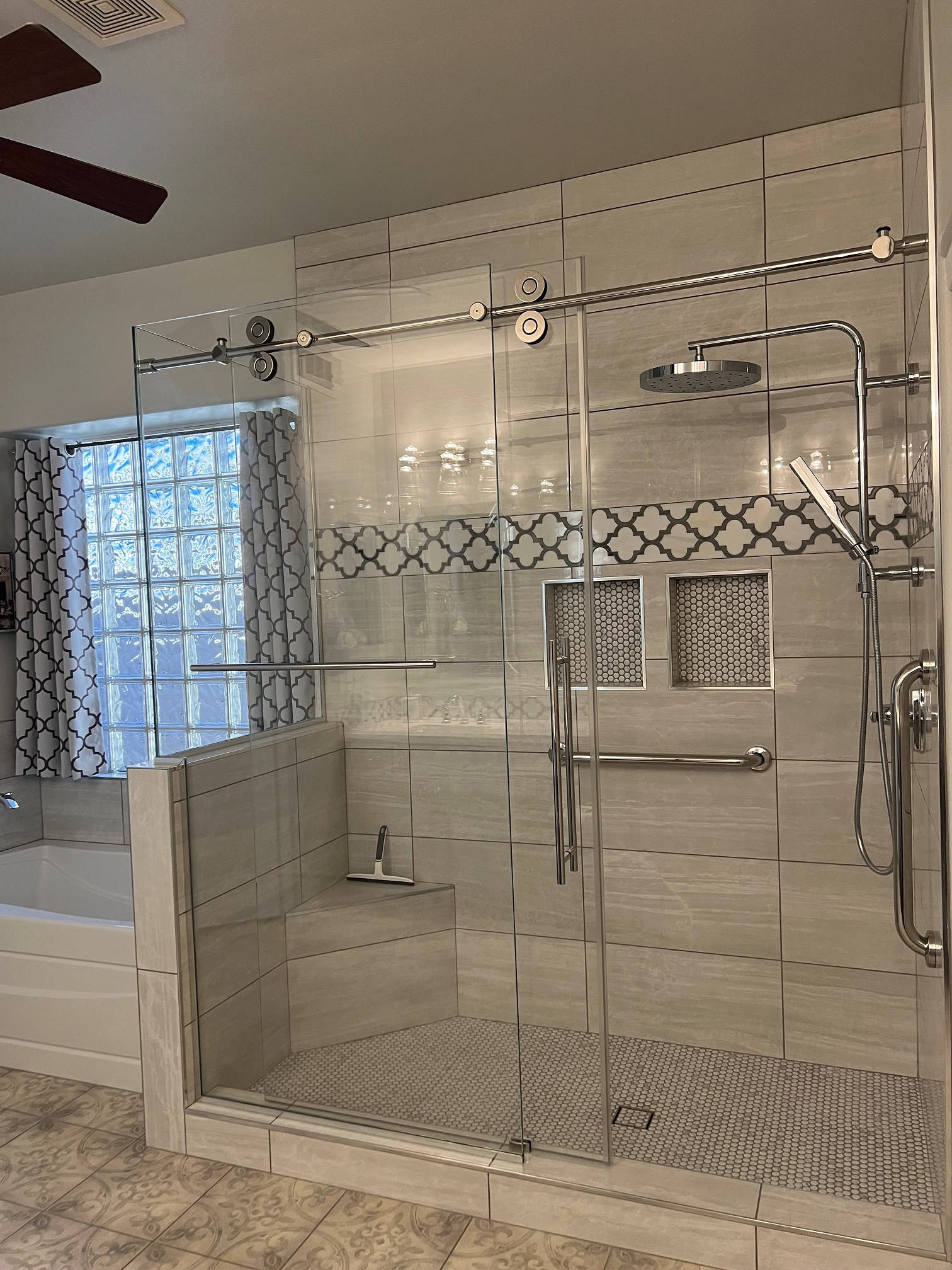 This Master Bathroom remodel is full of character and elegance with the decorative floor tile, spacious shower featuring 12" x 24" tile shower walls, penny tile floor and niche accents, glass surround with the barn door hardware, shower column and handheld in a bright chrome finish. [TWD Project Location: Surprise, AZ]