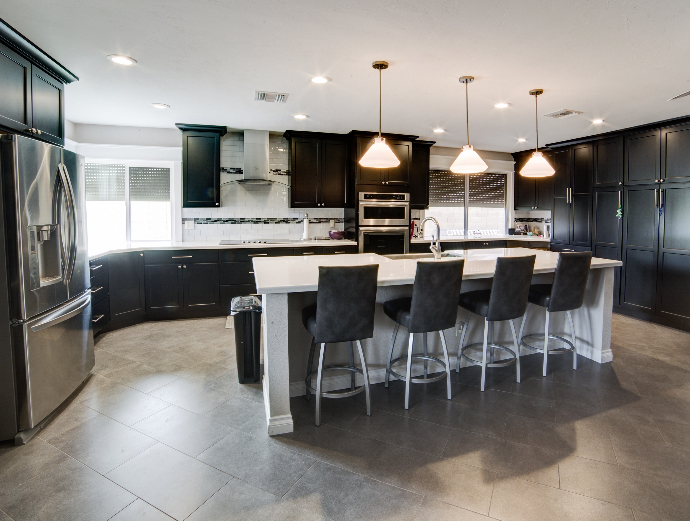 This designer gourmet kitchen remodel features Canyon Creek cabinetry with Brentwood doors and a Maple Ebony finish topped with Aleutian White Radianz Quartz counter tops and a Kohler Vault stainless steel farmhouse sink with coordinating fixtures, stainless steel and glass vent hood, and finished with a gorgeous trio of pendant lighting.    [TWD Project Location: Glendale, AZ]