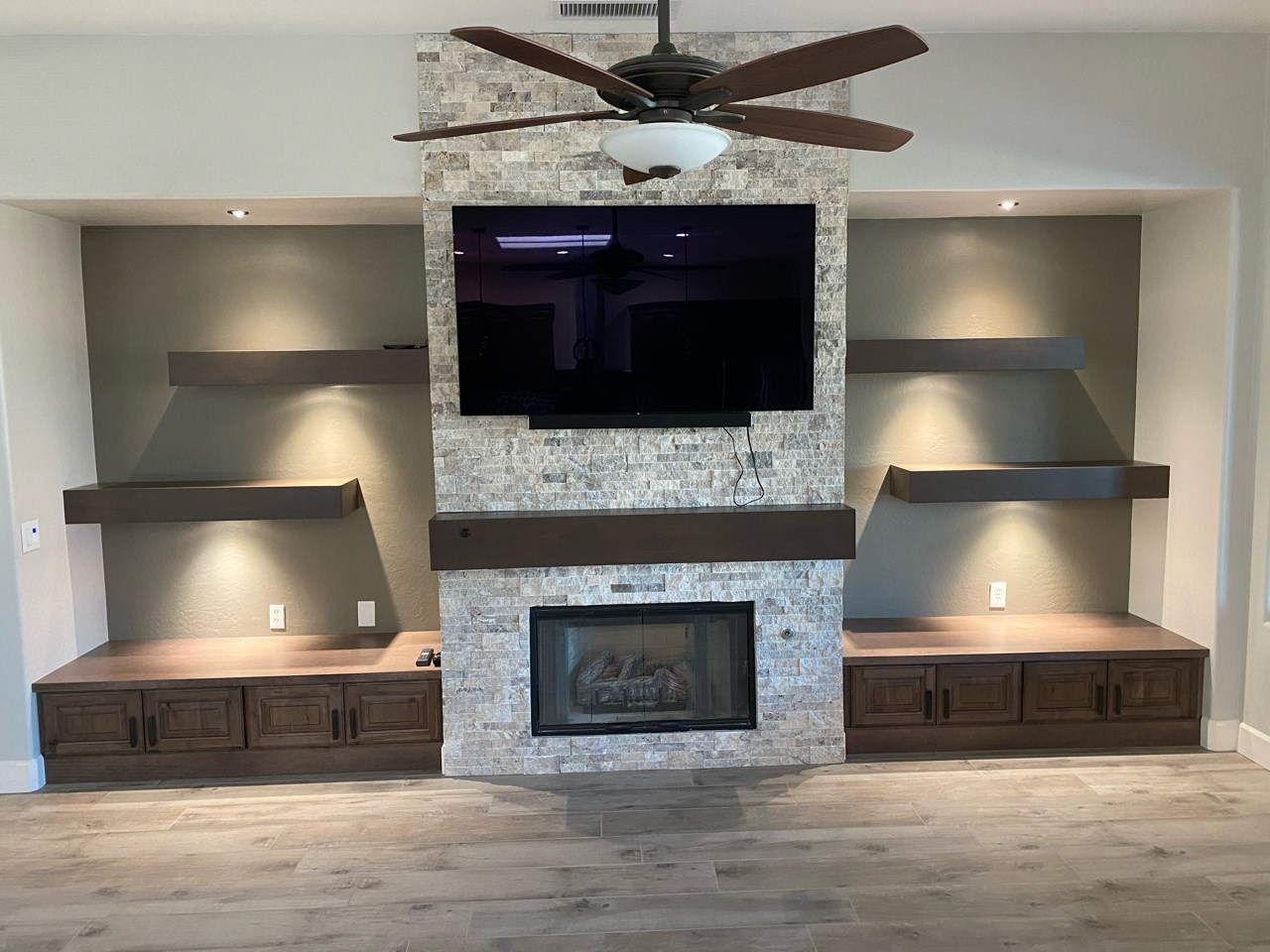 Stone feature wall, floating shelves, and Wellborn Cabinetry in Java color complete the look of this media wall. [TWD Project Location: Surprise, AZ]