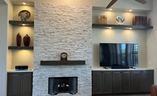 The stacked stone and floating shelves give this custom wall depth and character. The Maple Latte cabinetry from Waypoint Living Spaces help keep cords and other necessities stored out of sight. [TWD Project Location: Scottdale, AZ]