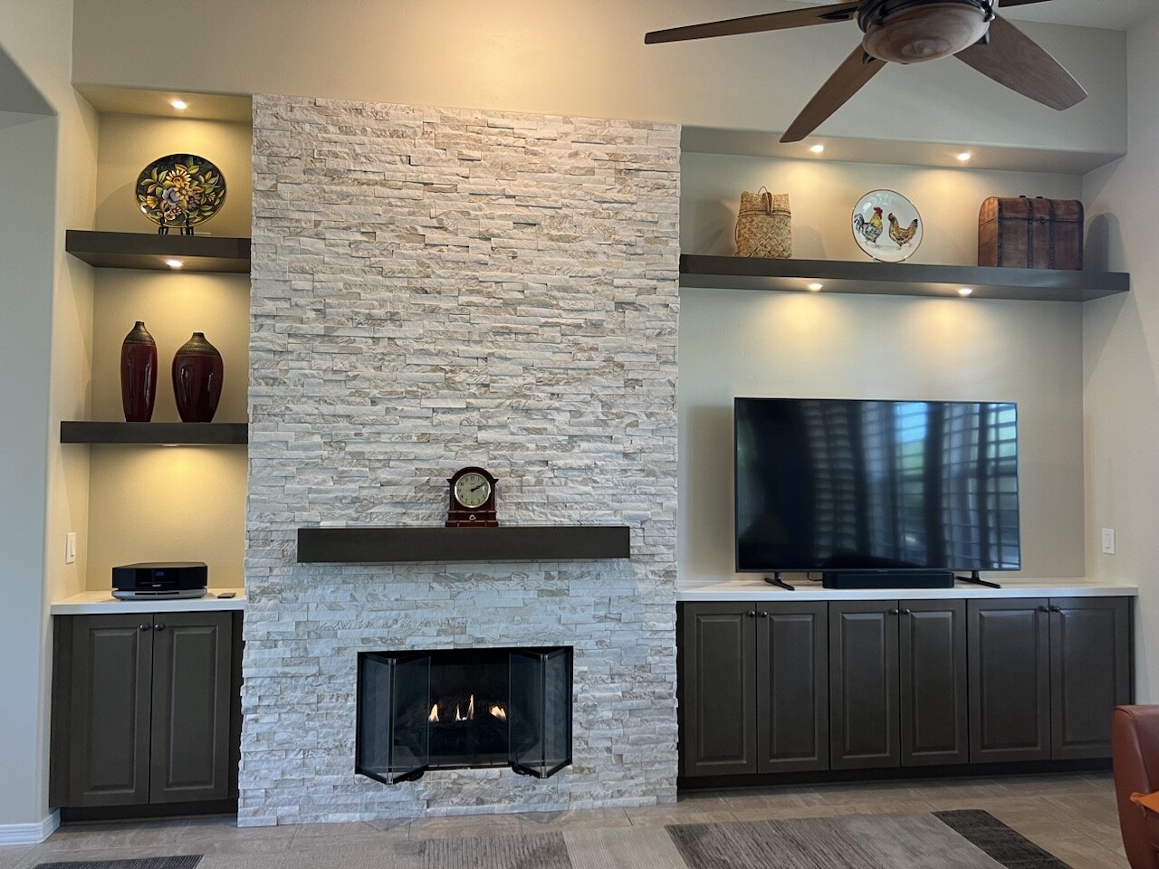 The stacked stone and floating shelves give this custom wall depth and character. The Maple Latte cabinetry from Waypoint Living Spaces help keep cords and other necessities stored out of sight. [TWD Project Location: Scottdale, AZ]