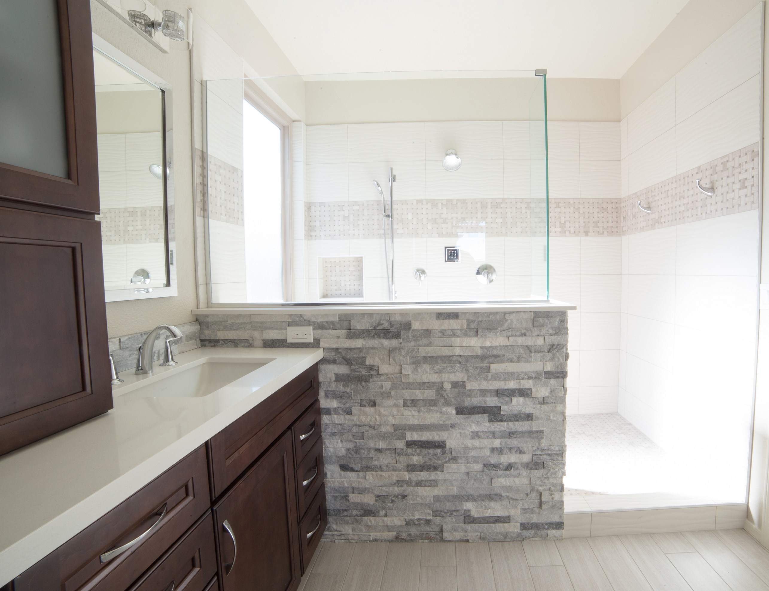 Gorgeous master bathroom remodel featuring multiple textures and neutral color palette in the spacious new walk-in shower, an interlocking stone lined pony wall and cherry wood double vanity topped with Snow White quartz. [TWD Project Location: Surprise, AZ]