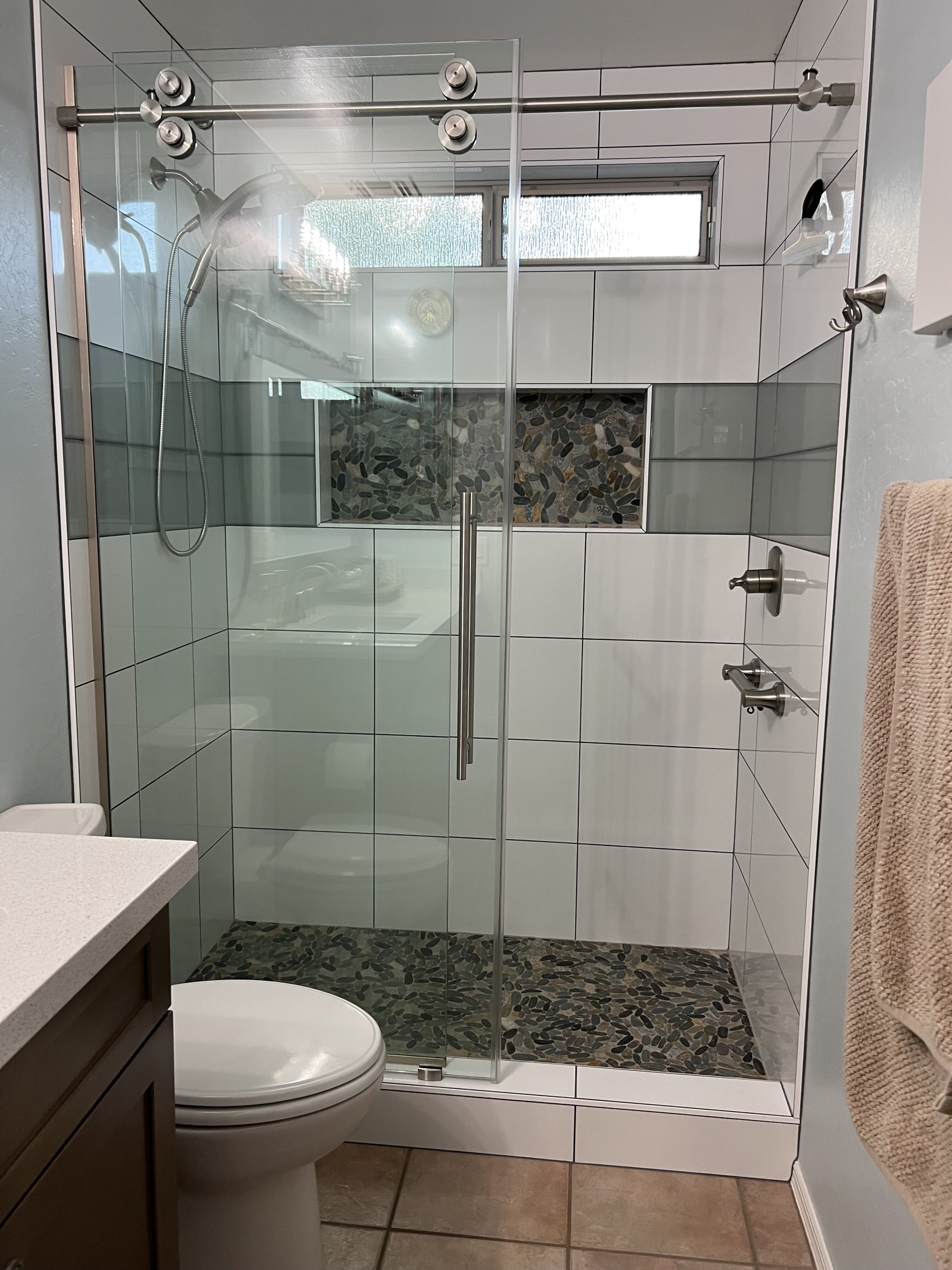 Taking the glossy 12" x 24" tile from floor to ceiling, adding in a mosaic pebble tile shower floor and sliding glass barn door truly make this hall bathroom remodel unique. [TWD Project Location: Glendale, AZ]