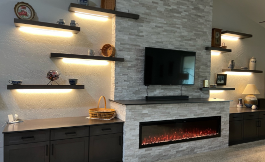 TWD framed out this custom media wall designed around the customers new electric fireplace as the focal point. This wall features upgraded electric, Waypoint Cabinetry in a Maple Slate finish, floating shelves with dimmable LED lighting and stacked stone installed to the top of the vaulted ceiling. [TWD Project Location: Goodyear, AZ]