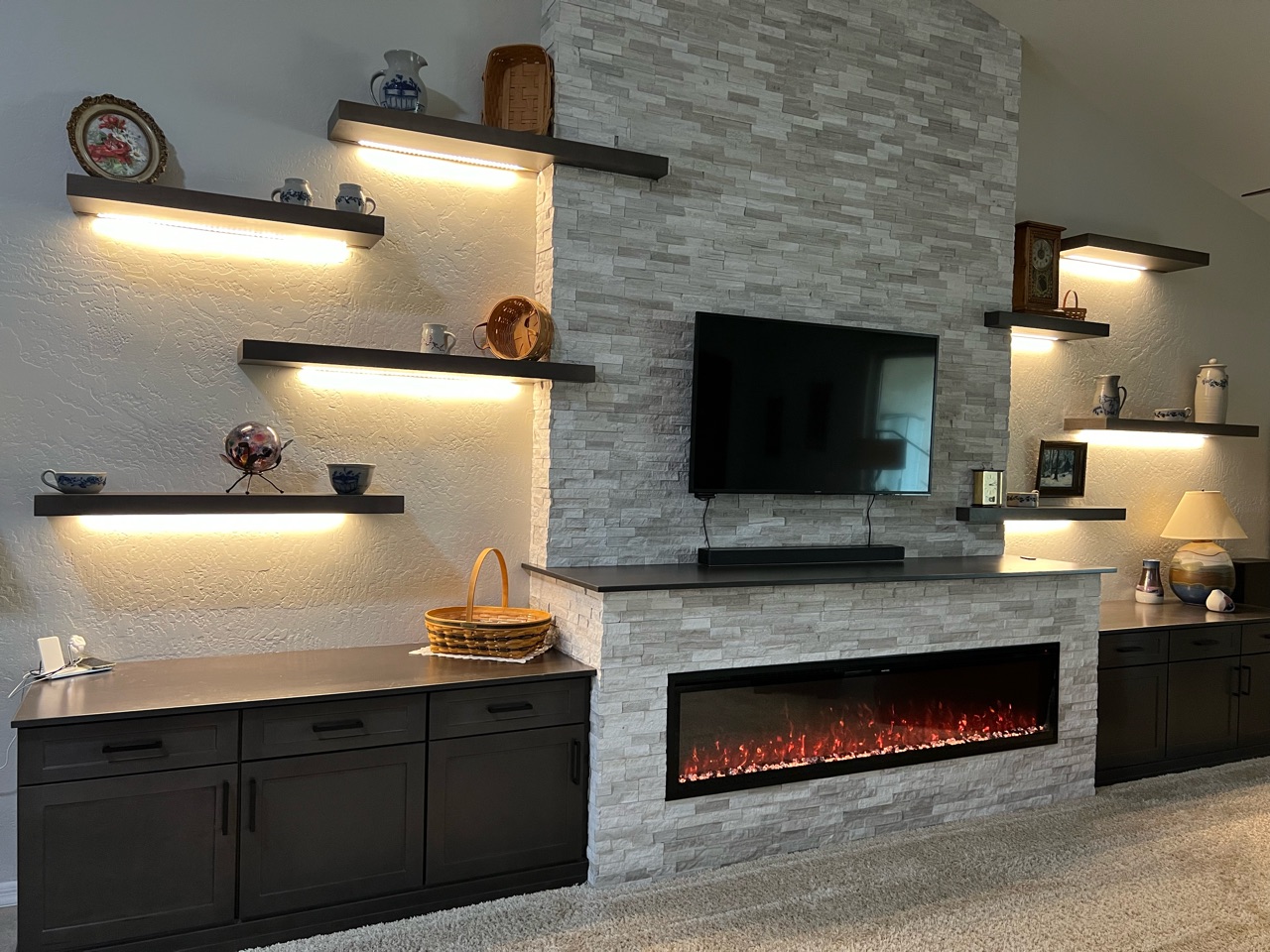 TWD framed out this custom media wall designed around the customers new electric fireplace as the focal point. This wall features upgraded electric, Waypoint Cabinetry in a Maple Slate finish, floating shelves with dimmable LED lighting and stacked stone installed to the top of the vaulted ceiling. [TWD Project Location: Goodyear, AZ]