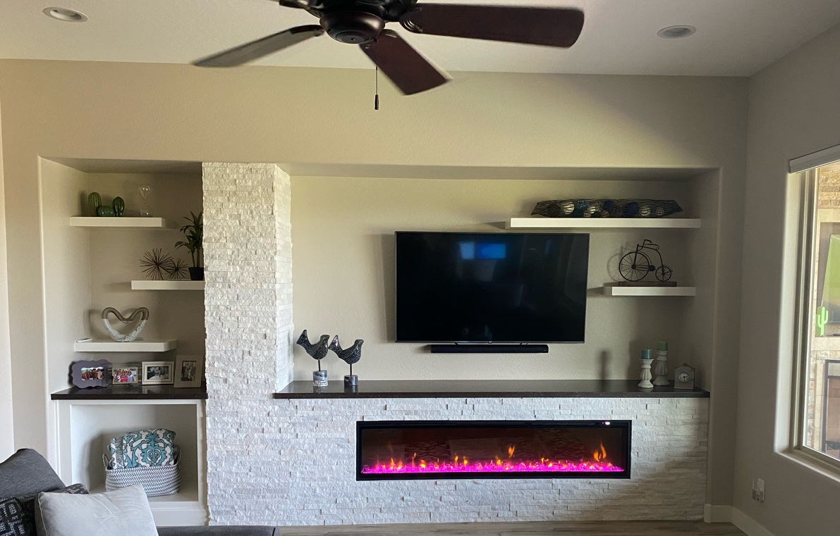 A custom media wall such as this is inclusive of TWD framing out the new design, electrical upgrades as needed, Wellborn Cabinetry floating shelves, Silestone quartz slab used on top of the cabinetry and the fireplace ledge, Artic White stone used around the fireplace and up the column, and the necessary additional support for the wall mounted television (fireplace supplied and installed by Others). [TWD Project Location: Peoria, AZ]