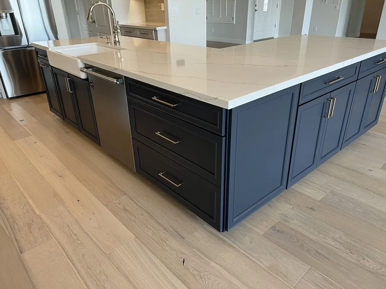 A modern kitchen island featuring sleek navy cabinets, brass hardware, and a polished quartz countertop with a farmhouse sink, offering functionality and style. Discover your dream kitchen today.