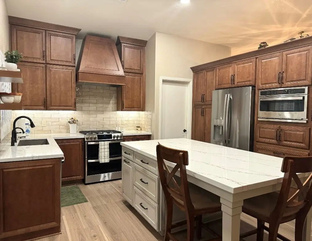 A warm and inviting kitchen featuring elegant wooden cabinets, a spacious white quartz island with seating, and modern stainless steel appliances. This functional and stylish space is perfect for hosting or daily family meals. Upgrade your kitchen today to blend comfort and sophistication.