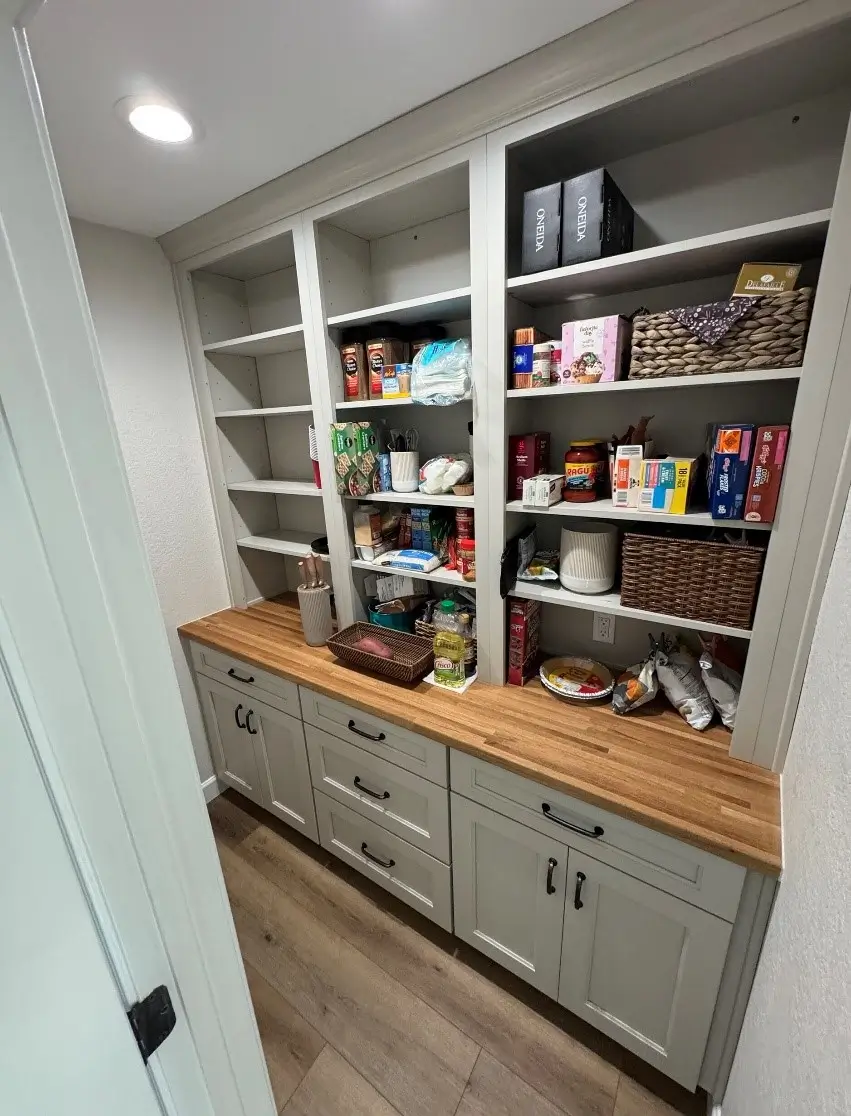 A neatly organized pantry featuring a wooden countertop with custom cabinets and open shelves, perfect for storing groceries, kitchen essentials, and decorative baskets. Upgrade your storage solutions today.