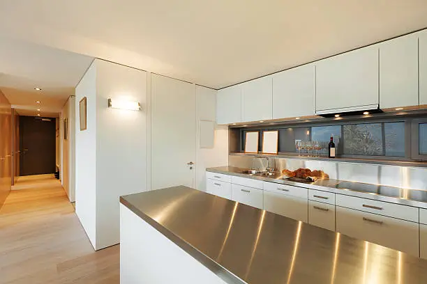 A modern kitchen featuring sleek stainless steel countertops and white cabinetry, reflecting a clean and minimalist design. The polished surface adds a contemporary touch while ensuring durability and hygiene.