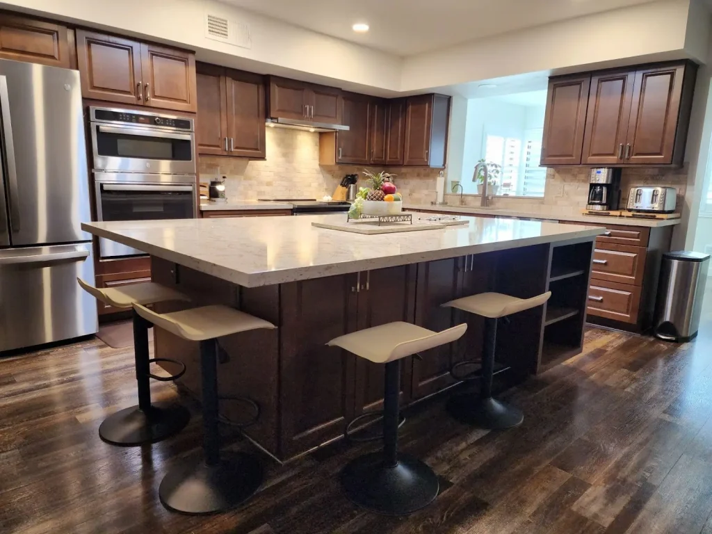 A beautifully designed kitchen featuring rich dark wood cabinetry, a spacious quartz countertop island with subtle veining, modern barstools, and stainless steel appliances for a sleek, contemporary feel.