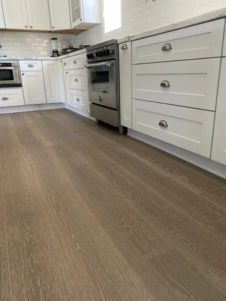 A modern kitchen with sleek white cabinetry, stainless steel appliances, and durable wood-look flooring, offering a stylish and functional space.