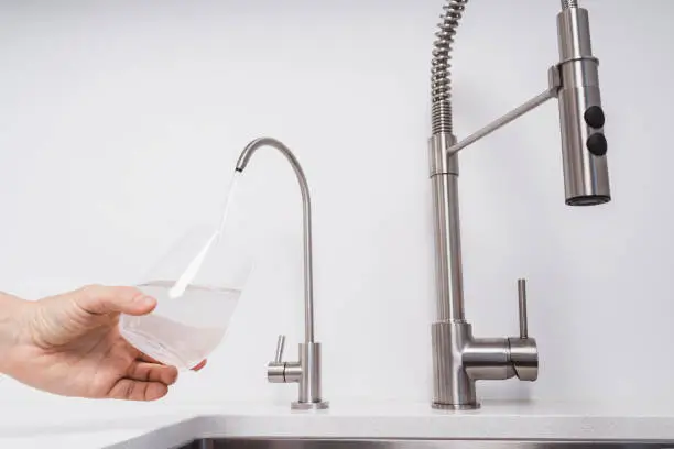 A sleek modern kitchen sink setup featuring a stainless steel pull-down faucet alongside a dedicated water filtration faucet, pouring clean drinking water into a glass.