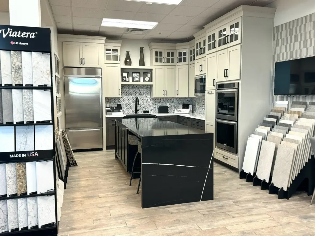 A modern kitchen showroom displaying a variety of countertop materials, featuring a black waterfall island, custom cabinetry, and stainless steel appliances.