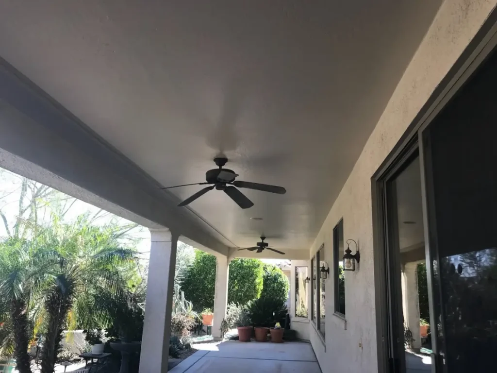 A covered patio with fresh stucco paint, ceiling fans, and lush greenery, creating a relaxing outdoor space.