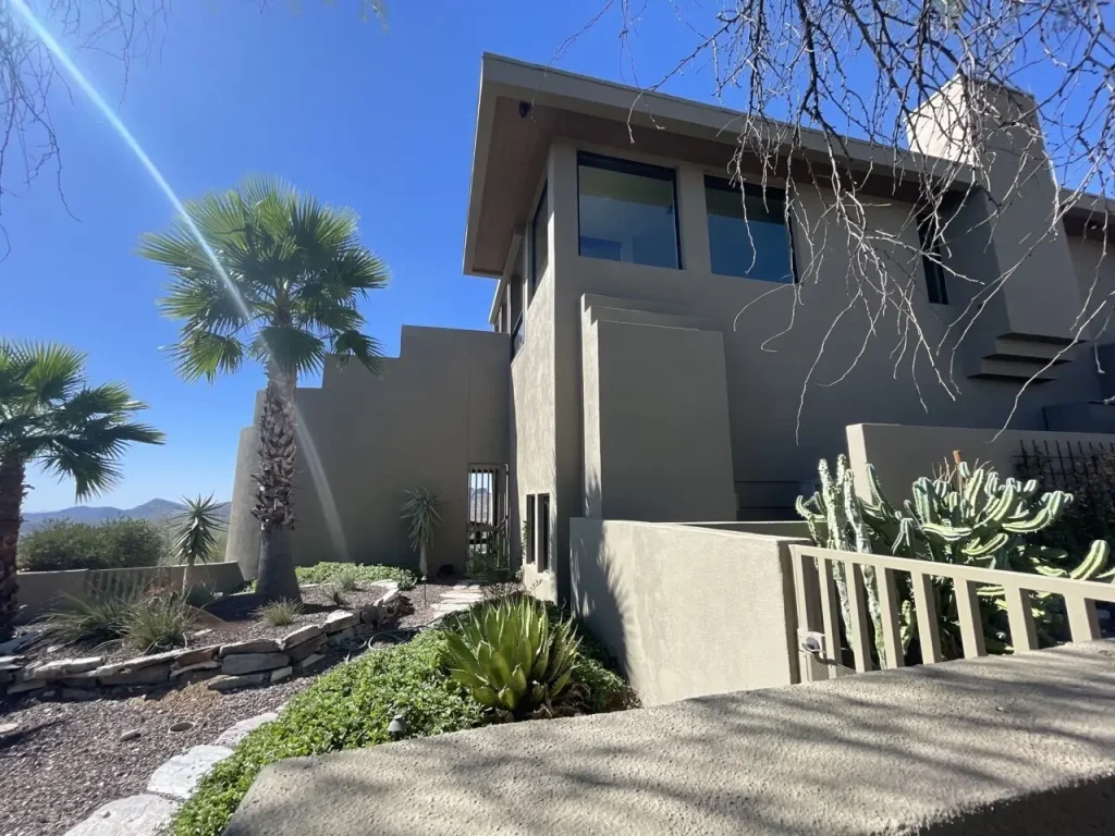 A modern desert home with fresh stucco paint, surrounded by lush desert landscaping, palm trees, and a bright blue sky.