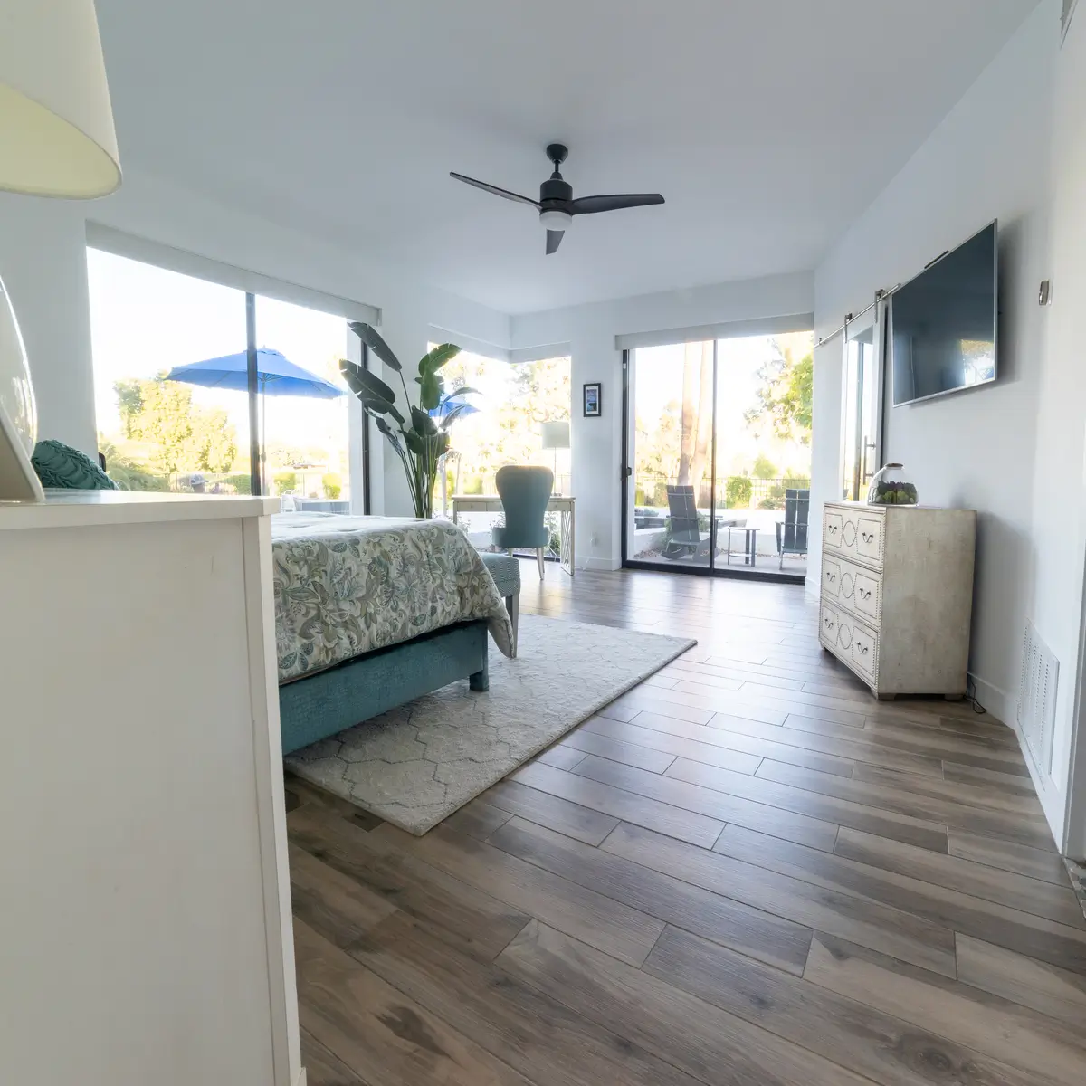 Modern bedroom with smooth drywall finishes, wood-look tile flooring, and large glass doors opening to a patio.