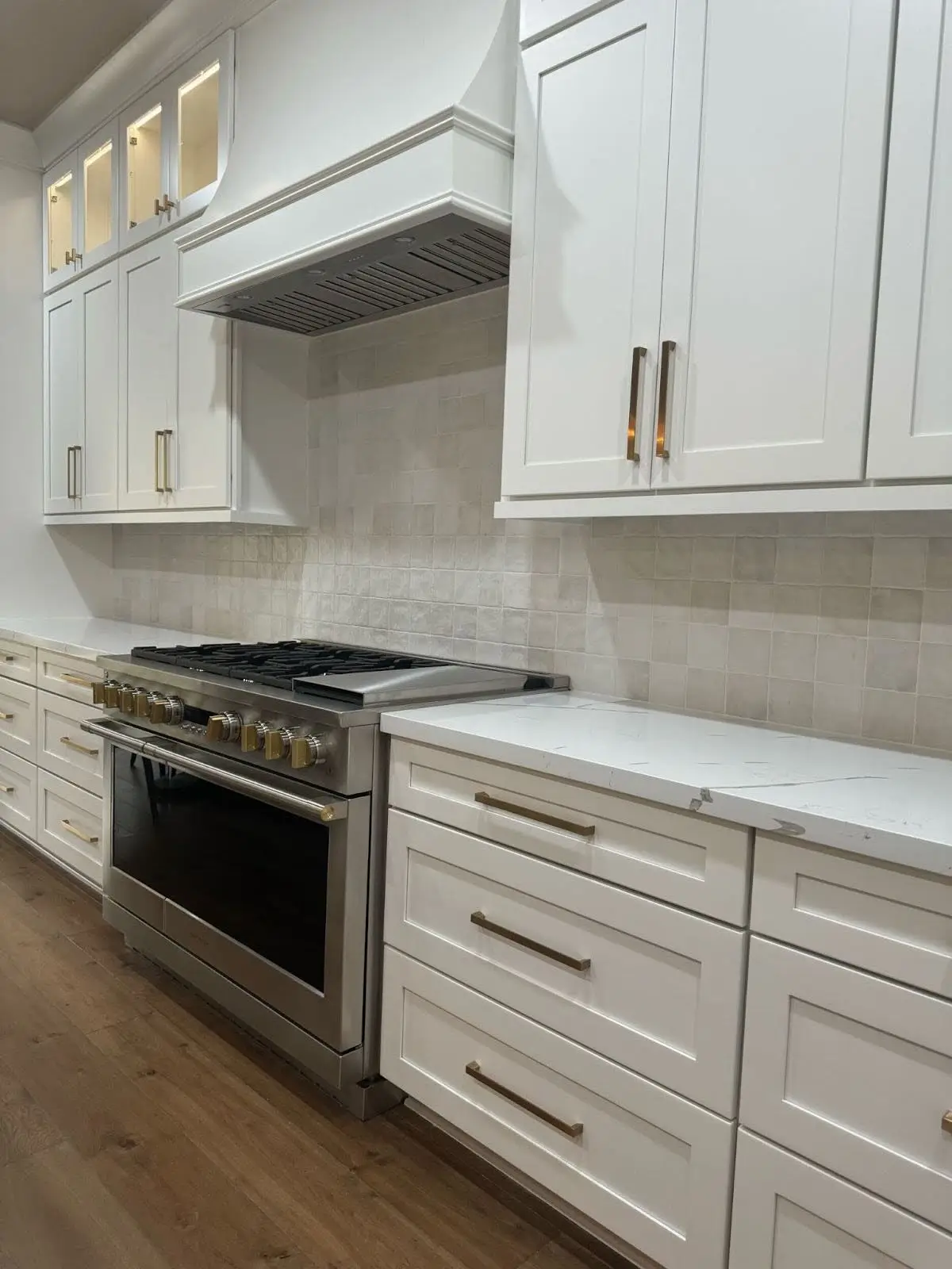 Modern kitchen with a stainless steel gas stove, white shaker cabinets, and a minimalist tile backsplash.