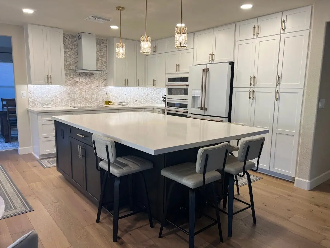 Modern kitchen with heated hardwood flooring, a large kitchen island, and white cabinetry, illuminated by pendant lights.