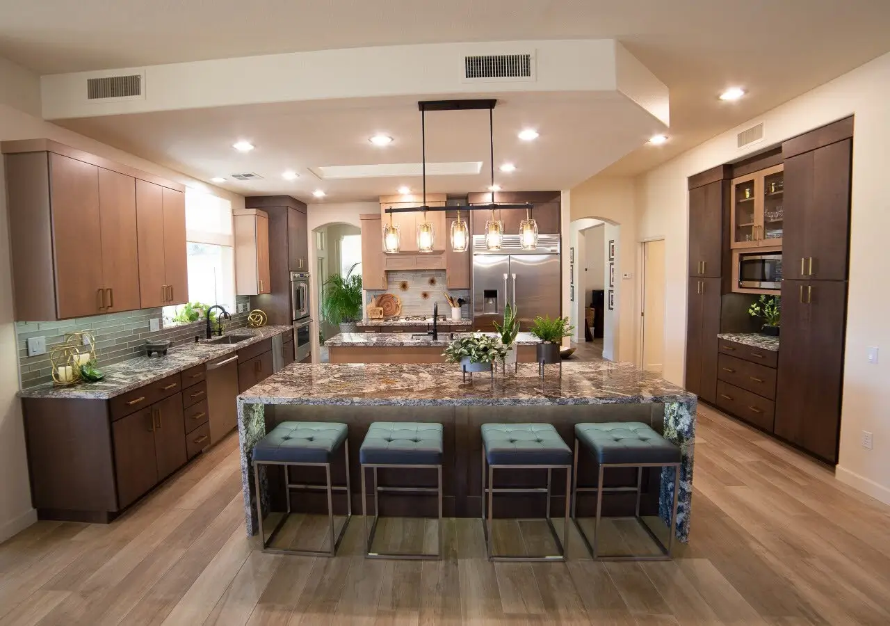 Modern kitchen interior featuring wood-look tile flooring, granite countertops, pendant lighting, and brown cabinetry with a central island and barstools.