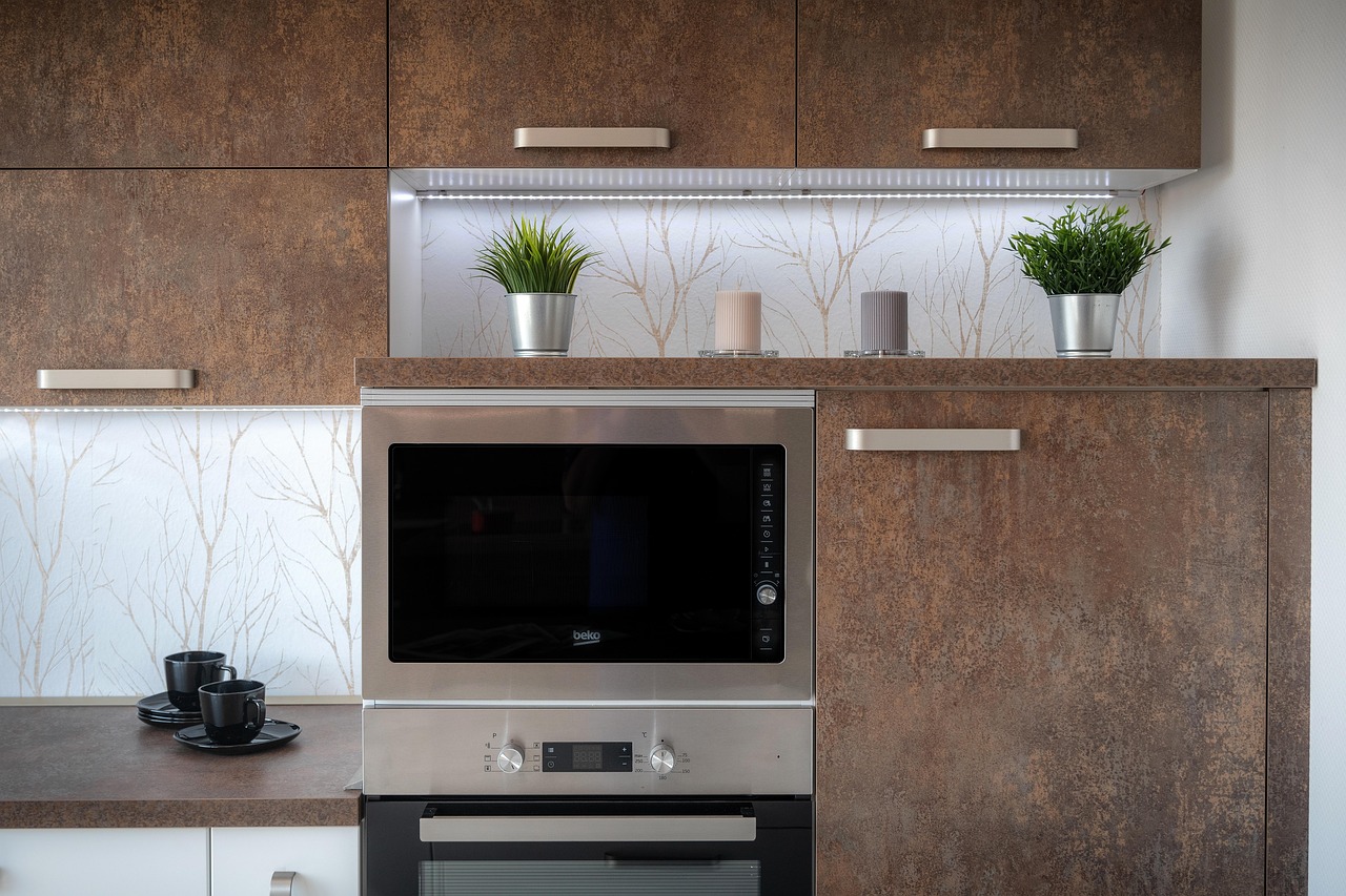 Modern kitchen with built-in stainless steel microwave and oven set against textured wooden cabinets, accented by decorative plants and candles.