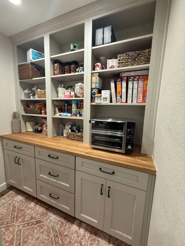 Built-in kitchen pantry with open shelving, wooden countertop, and organized food storage in a modern kitchen design.