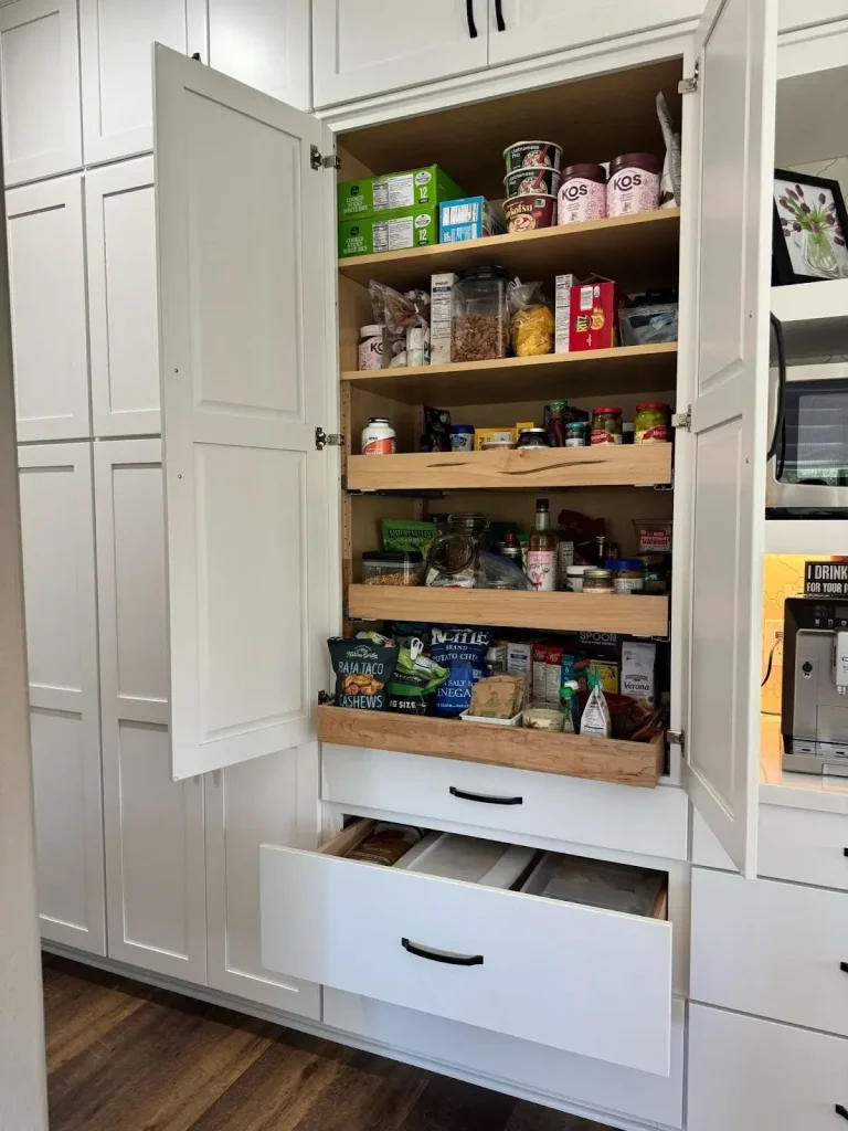 Modern kitchen pantry with pull-out wooden shelves and spacious drawers for organized food storage in a compact kitchen.