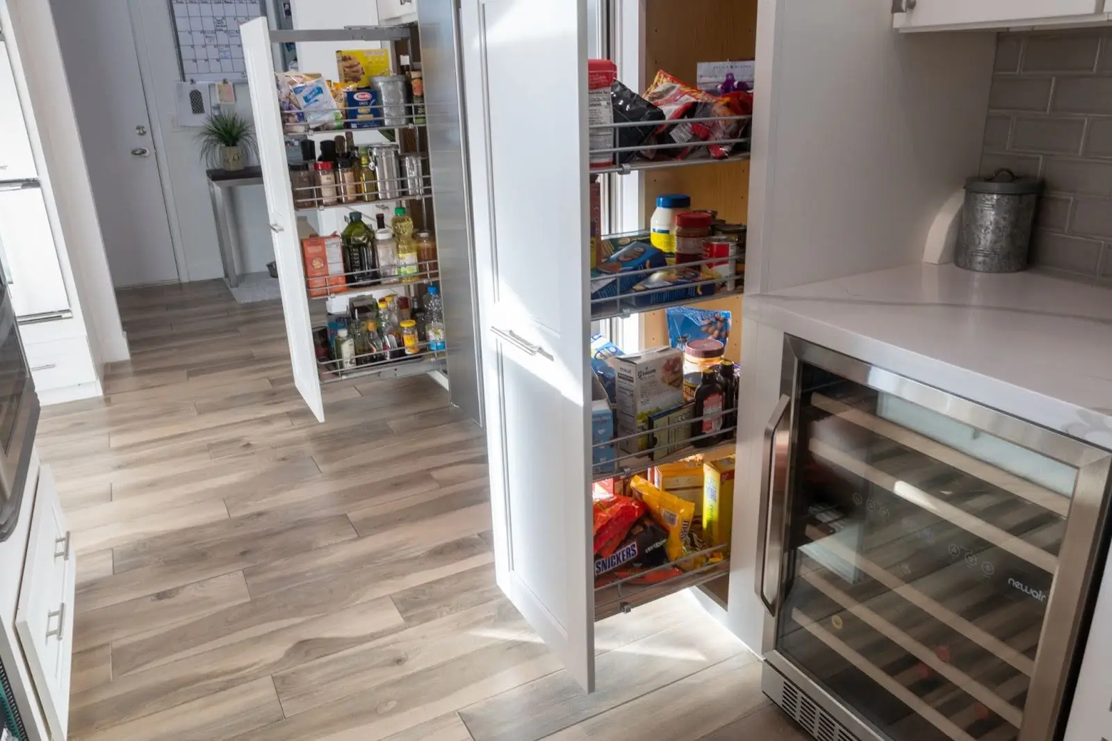 Open pull-out pantry shelves with organized food items and kitchen essentials in a modern kitchen with wooden flooring.